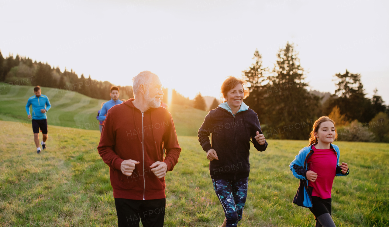 A large group of people cross country running in nature at sunset.