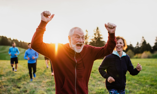 A large group of people cross country running in nature at sunset.