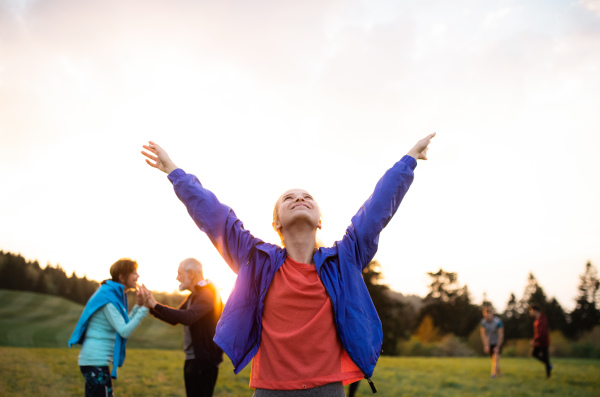 A portrait of young woman with large group of people doing exercise in nature, resting.