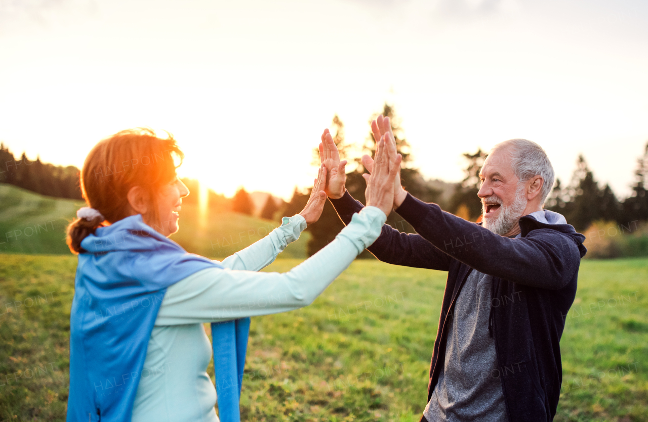 An active and fit senior couple resting after doing exercise in nature at sunset.