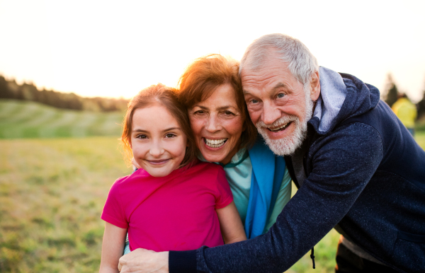 An active senior couple with granddaughter standing in nature at sunset, looking at camera.