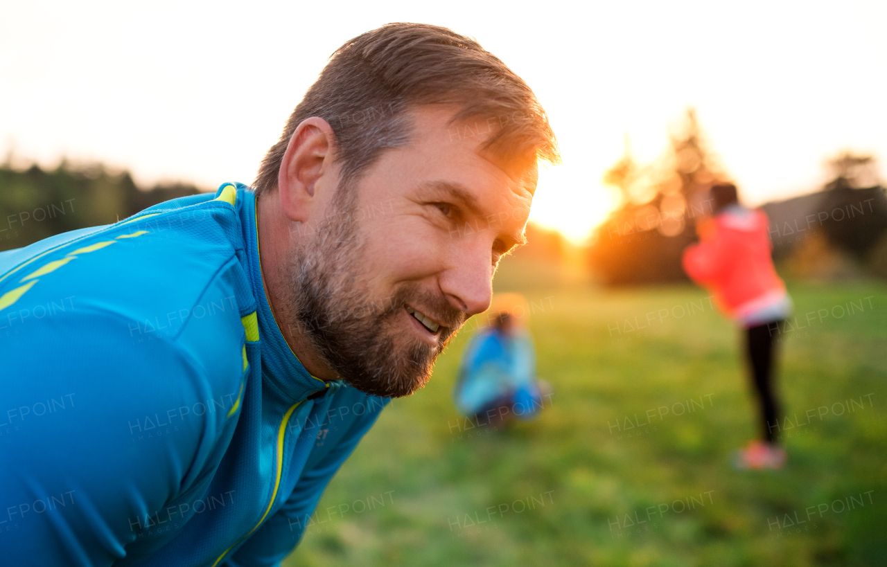 A portrait of young man with large group of people doing exercise in nature, resting.