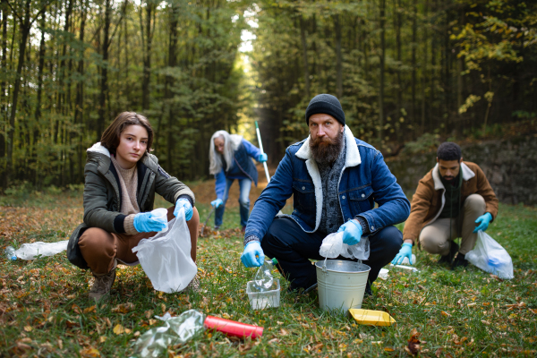 A group of volunteers looking at camera and cleaning up forest from waste, community service concept