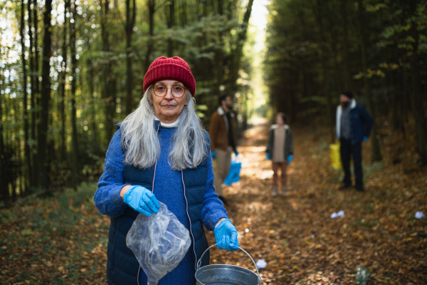 A senior woman volunteer looking at camera when cleaning up forest from waste, community service.