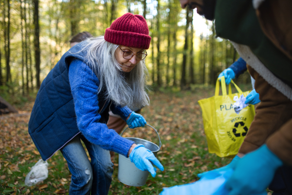 A senior woman volunteer cleaning up forest from waste, community service concept.