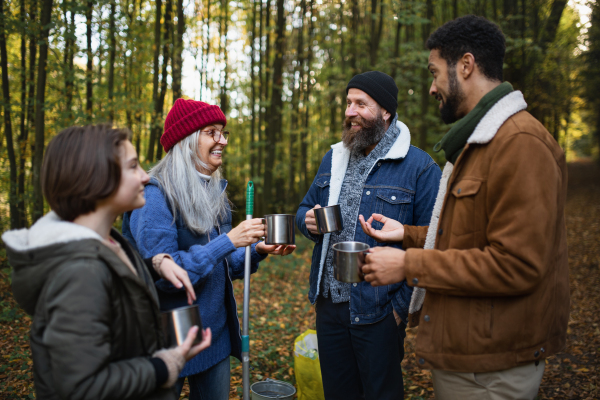 A diverse group of happy volunteers cleaning up forest, having break, drinking tea and talk together.