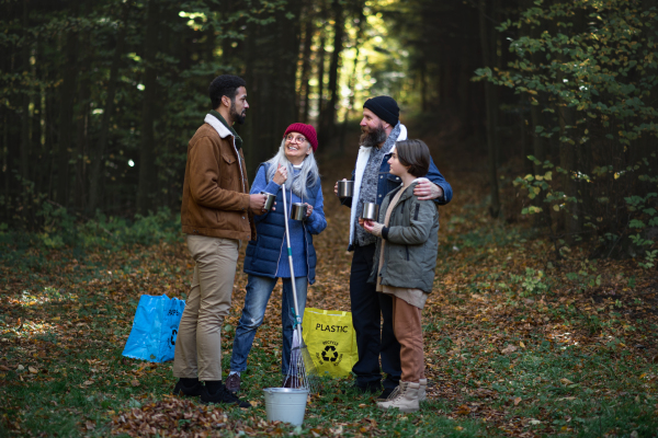 A diverse group of happy volunteers cleaning up forest, having break, drinking tea and talk together.