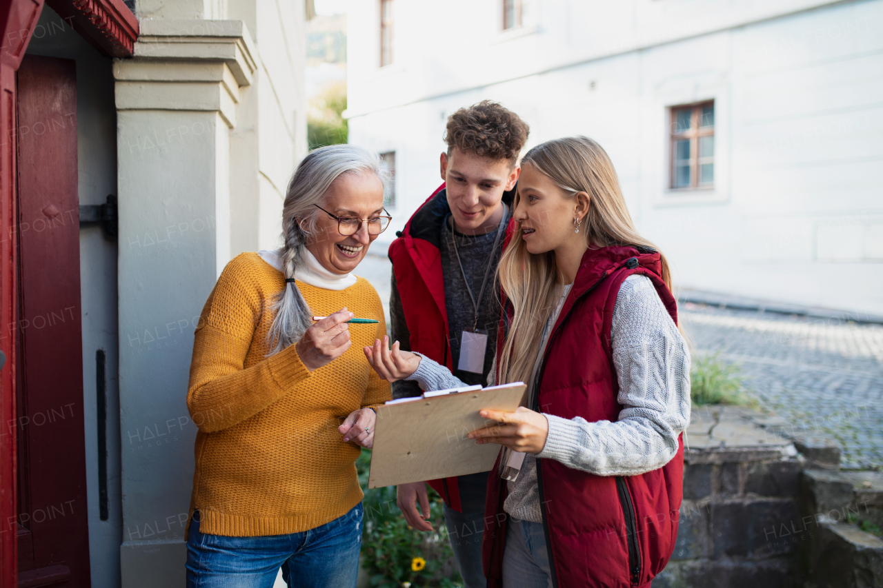 Young door to door volunteers talking to senior woman and taking a survey at her front door.