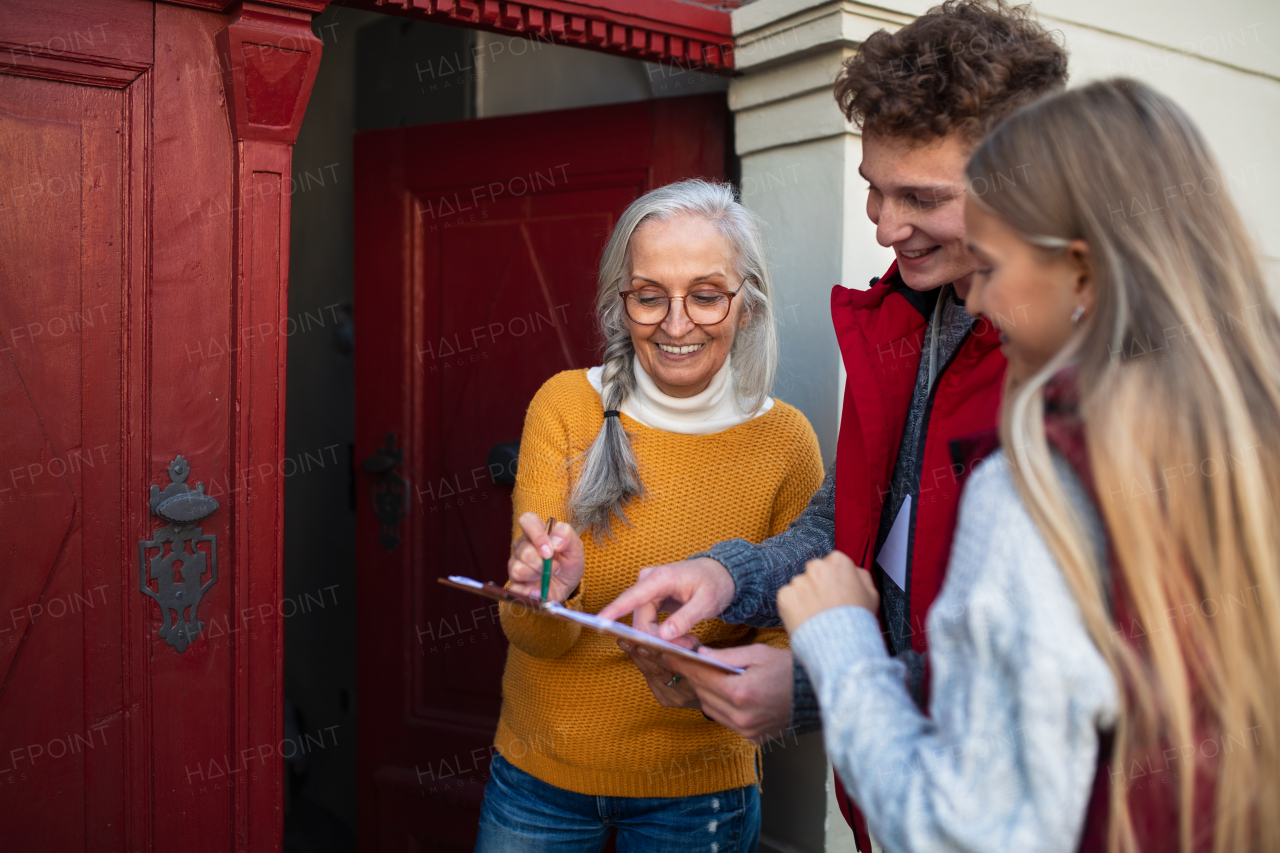 Young door to door volunteers talking to senior woman and taking a survey at her front door.