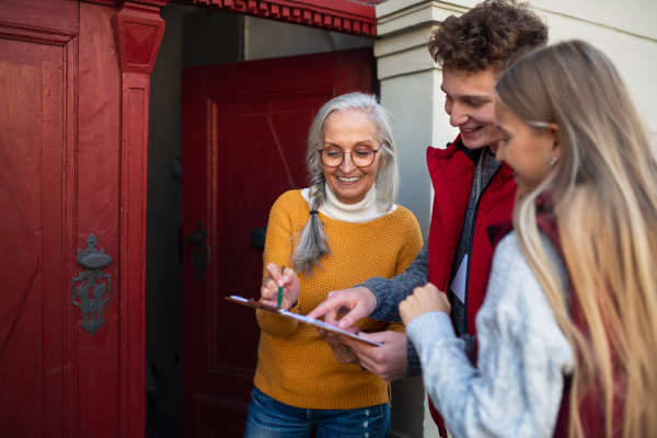 Young door to door volunteers talking to senior woman and taking a survey at her front door.