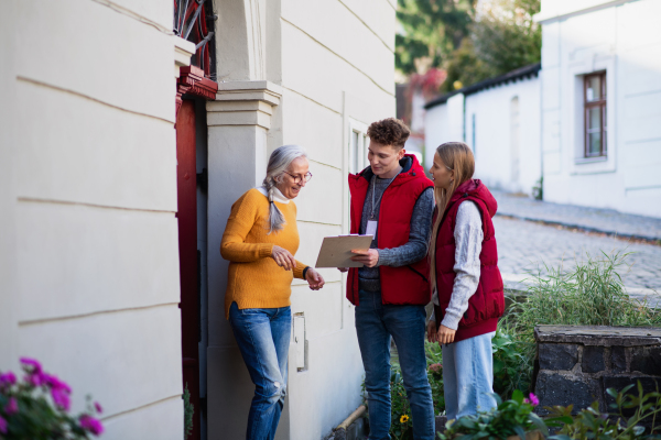 Young door to door volunteers talking to senior woman and taking a survey at her front door.