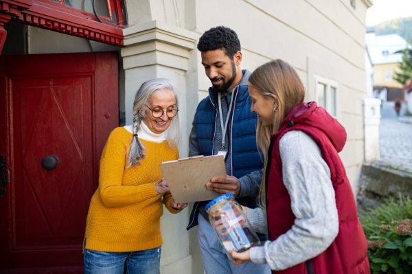 Young door to door fundraisers talking to senior woman and collecting money for charity in a street.