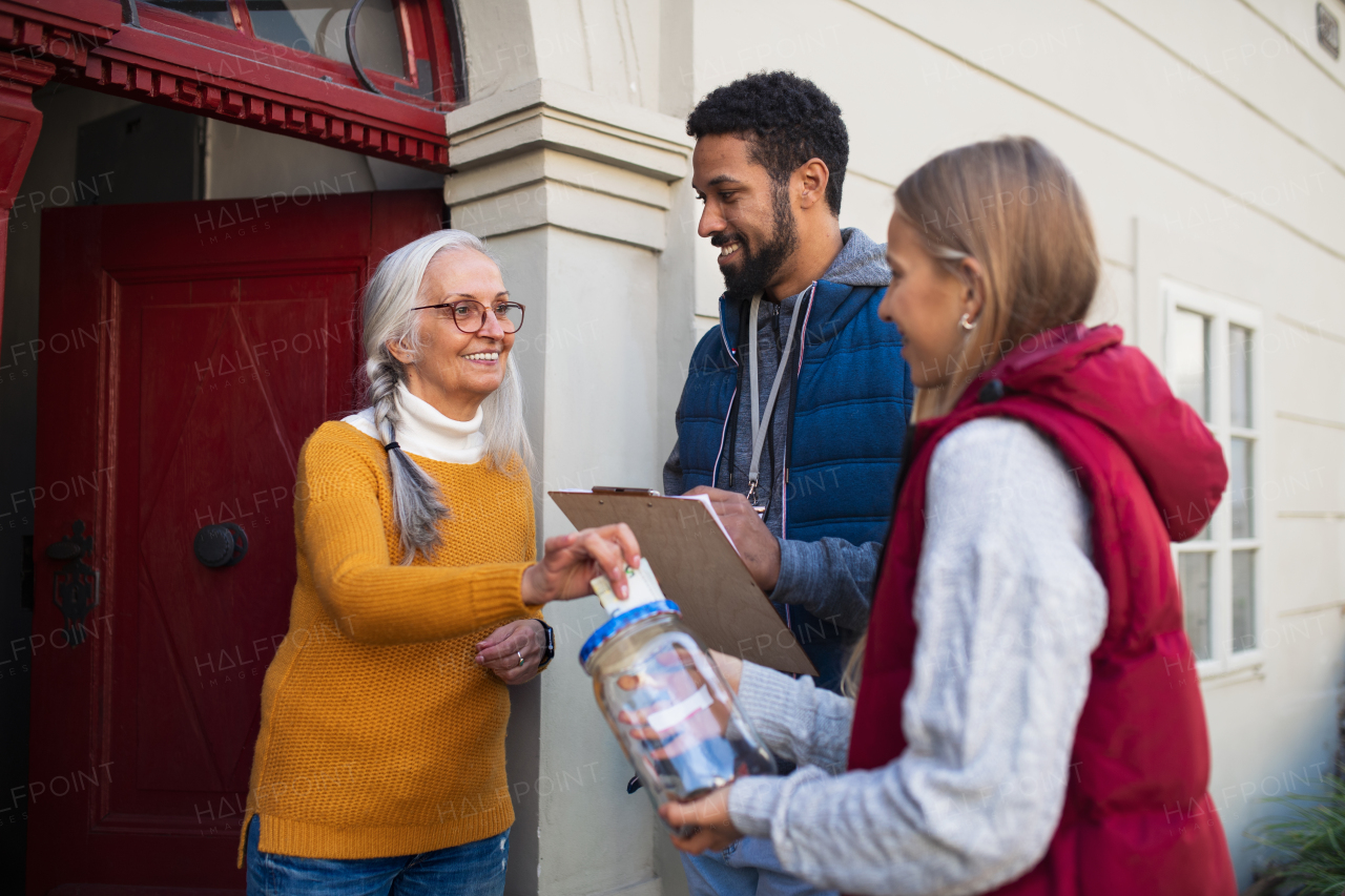 Young door to door fundraisers talking to senior woman and collecting money for charity in a street.