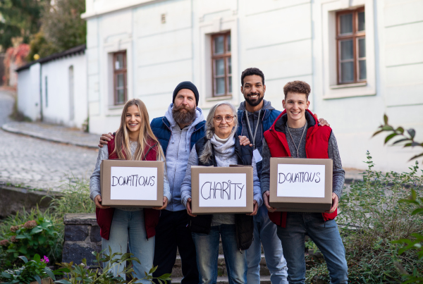 A diverse group of volunteers with donation boxes standing outdoors, social care and charity concept