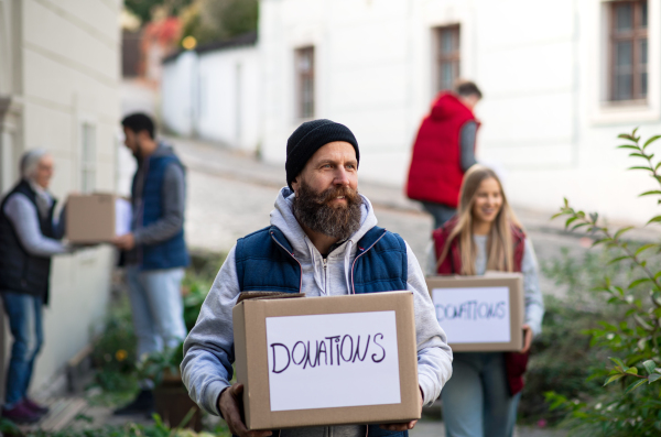 A diverse group of volunteers with donation boxes standing outdoors, social care and charity concept