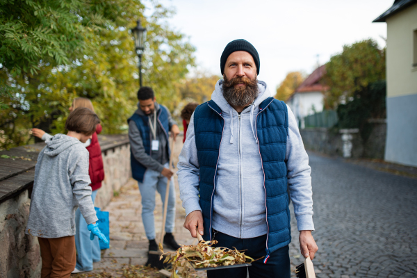 A mature man volunteer with team looking at camera and cleaning up street, community service concept