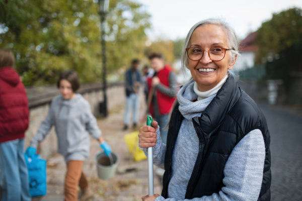 Happy senior woman volunteer with team cleaning up street, community service concept