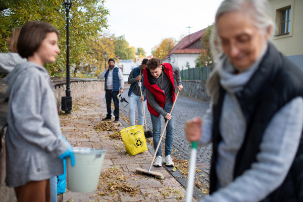 A diverse group of happy volunteers cleaning up street, community service concept