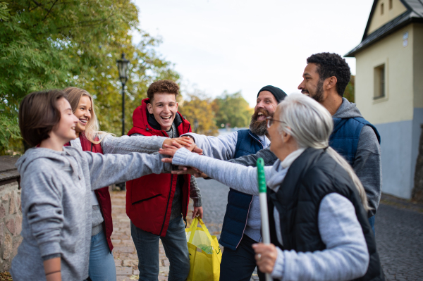 A diverse group of happy community service volunteers stacking hands together outdoors in street