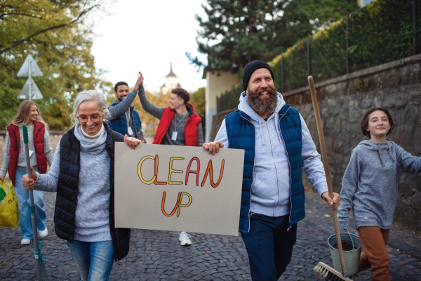 A diverse group of happy volunteers walking with banner and tools to do street clean up.