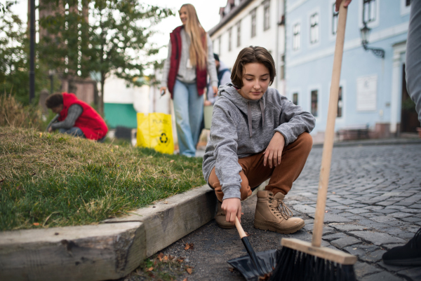 A preteen girl volunteer with team cleaning up street, community service concept