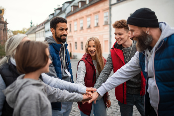 A diverse group of happy community service volunteers stacking hands together outdoors in street