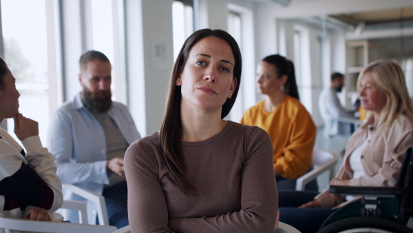 A group of people on therapy session, depressed woman looking at camera.