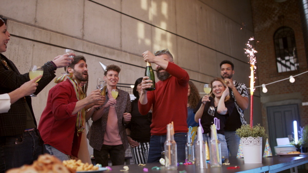 A large group of colleagues having a big party in office, opening champagne.