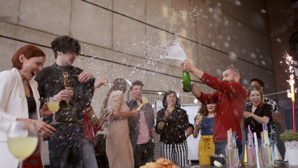 A large group of colleagues having a big party in office, opening champagne.