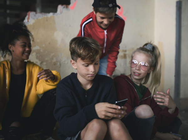 Front view of group of teenagers gang sitting indoors in abandoned building, using smartphones.