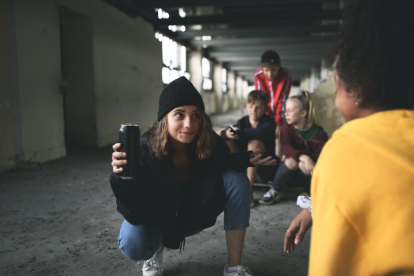 Front view of group of teenagers gang sitting indoors in abandoned building, using smartphones.