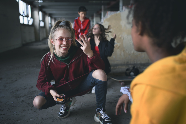 Front view of group of teenagers gang sitting indoors in abandoned building, using smartphones.