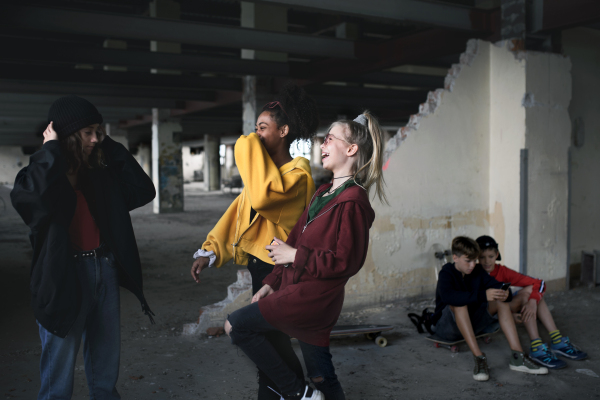 Group of cheerful teenagers gang sitting indoors in abandoned building, having fun.