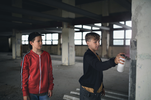 Group of teenagers boy gang standing indoors in abandoned building, using spray paint on wall.