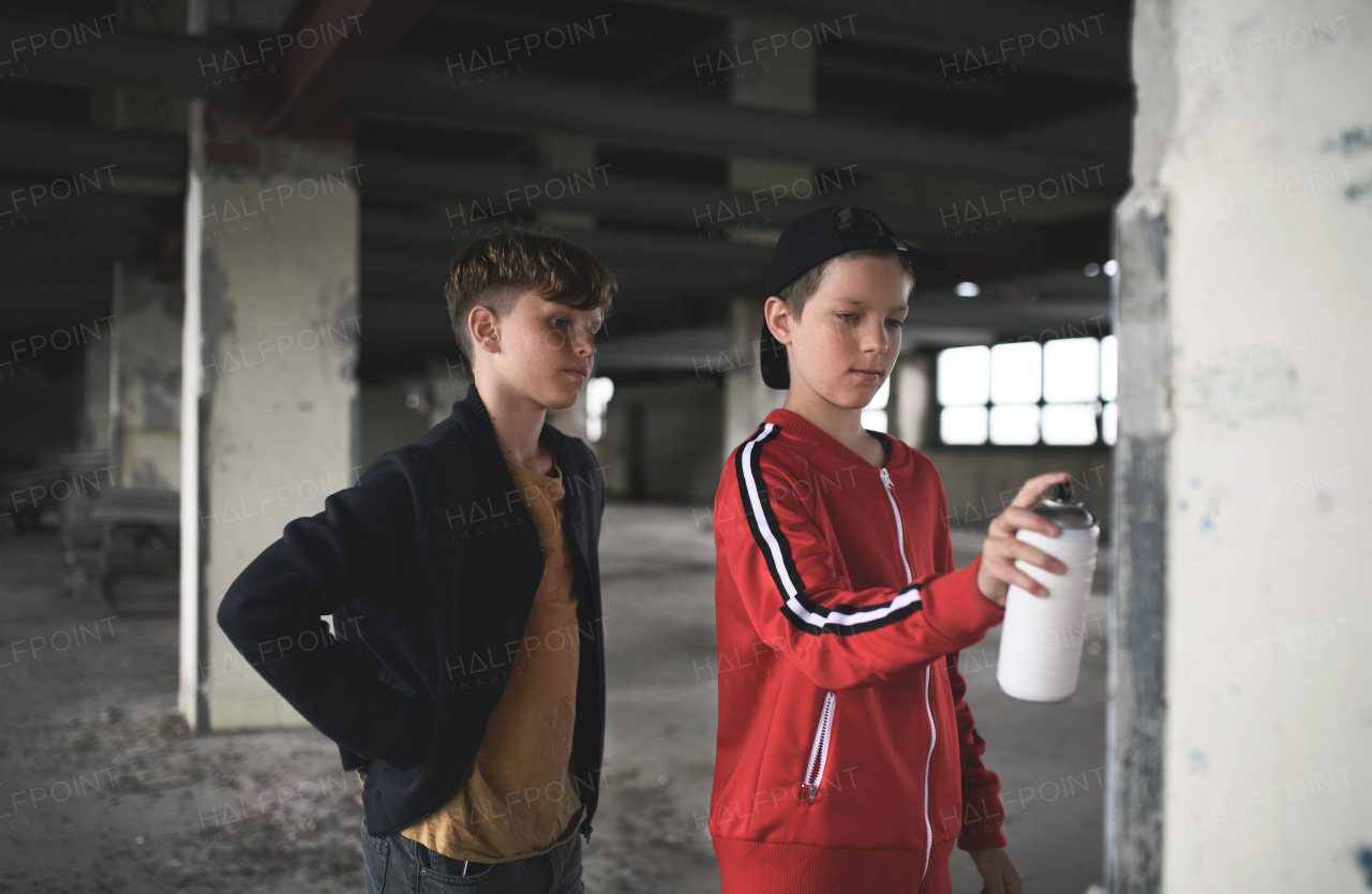 Group of teenagers boy gang standing indoors in abandoned building, using spray paint on wall.