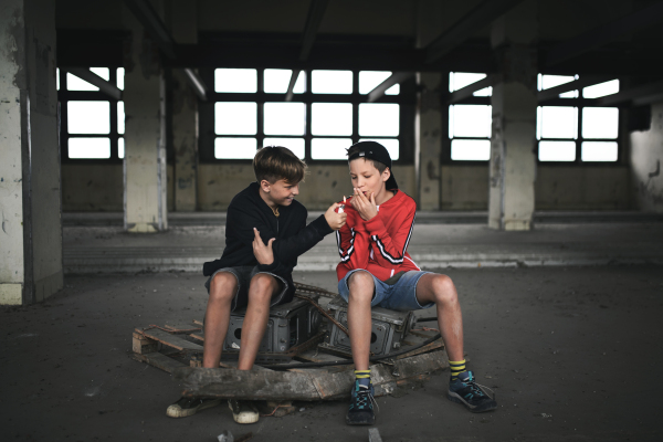 Group of teenagers boys gang indoors in abandoned building, smoking cigarettes.