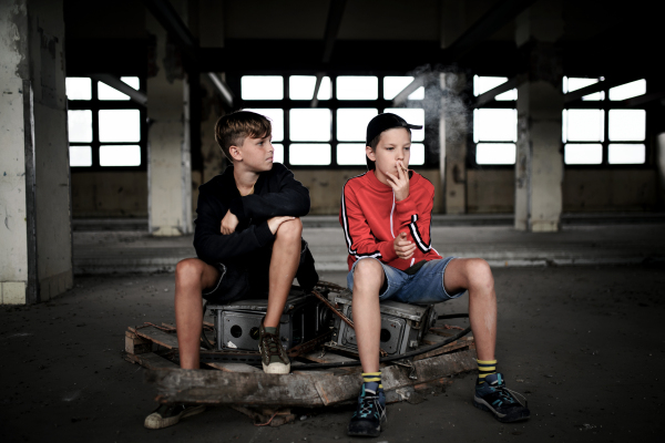 Group of teenagers boys gang indoors in abandoned building, smoking cigarettes.