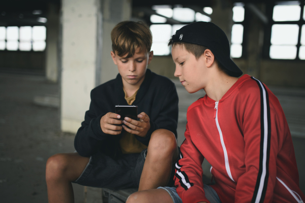 Group of teenagers boys gang indoors in abandoned building, using smartphone.