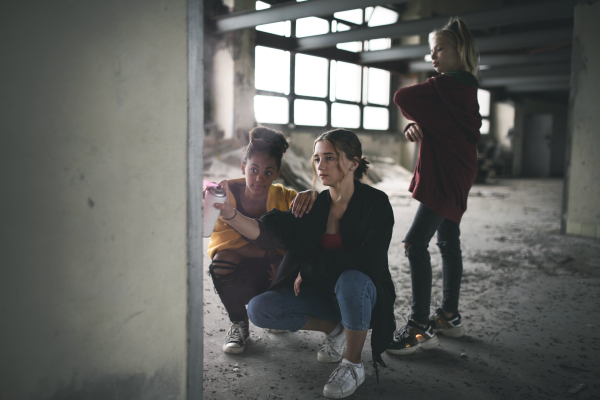 Group of teenagers girl gang standing indoors in abandoned building, using spray paint on wall.