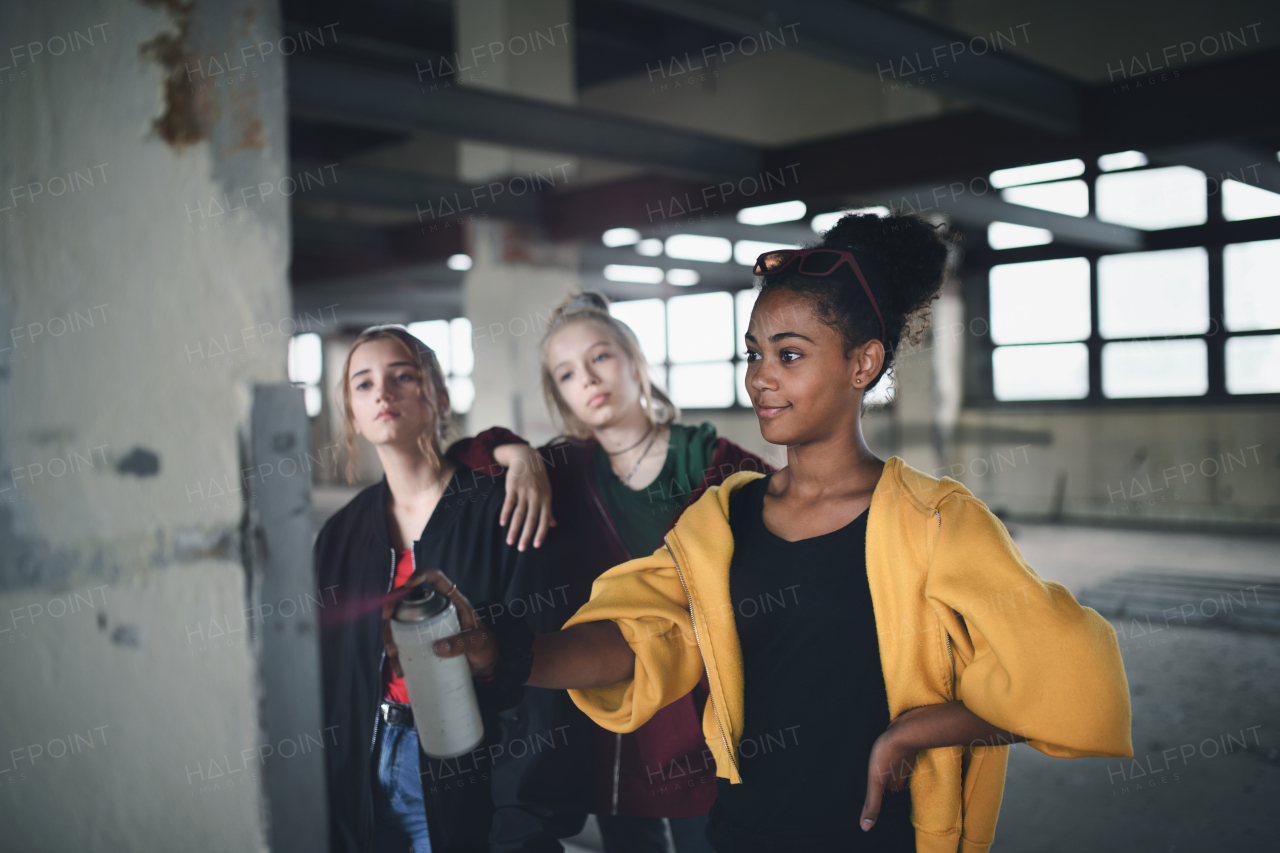 Group of teenagers girl gang standing indoors in abandoned building, using spray paint on wall.