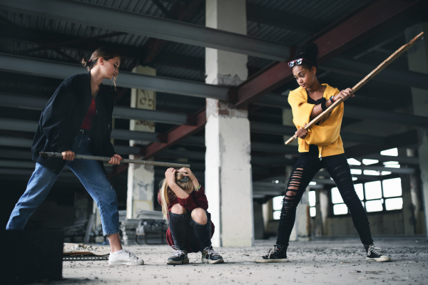 Scared teenage girl attacked by thugs in abandoned building, gang violence and bullying concept.