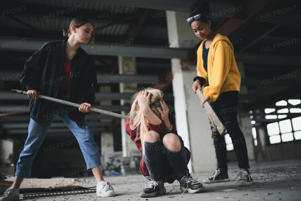 Scared teenage girl attacked by thugs in abandoned building, gang violence and bullying concept.