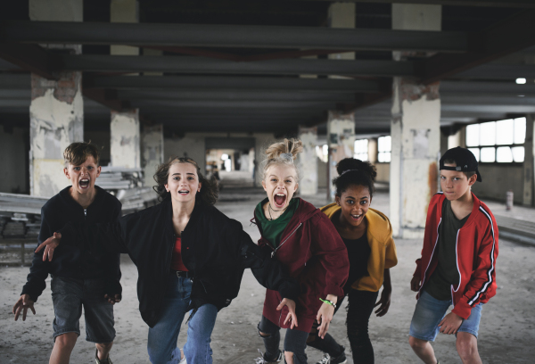 Front view of group of teenagers girl gang standing indoors in abandoned building, shouting at camera.