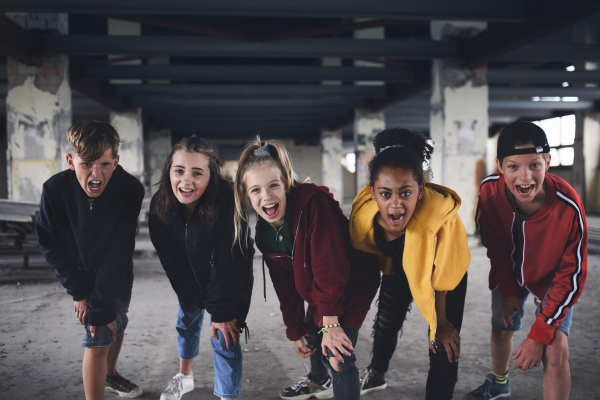 Front view of group of teenagers gang standing indoors in abandoned building, looking at camera.