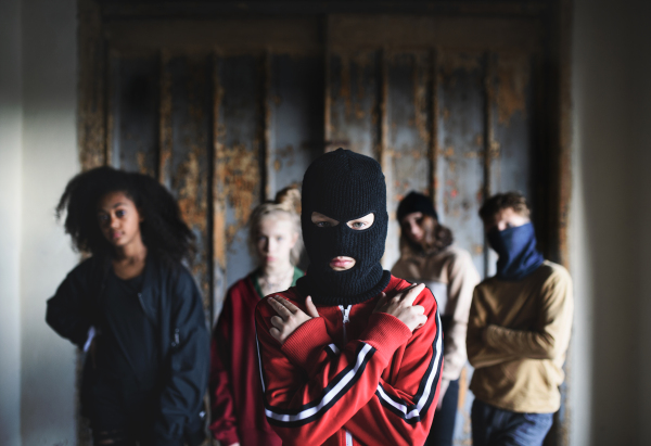 Boy with mask with teenagers gang standing indoors in abandoned building, showing finger gun gesture.