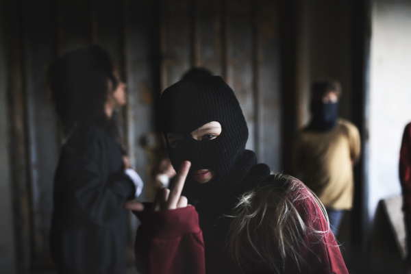 Girl with face mask from teenagers gang standing indoors in abandoned building, showing middle finger.