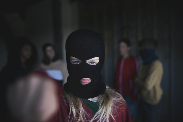 Girl with mask from teenagers gang standing indoors in abandoned building, attacking with fist gesture.