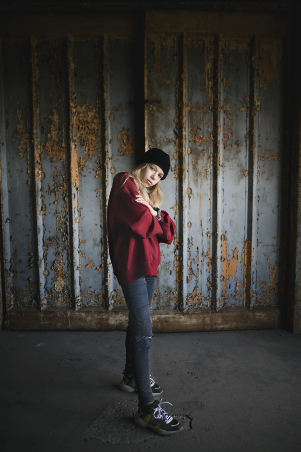 Front view portrait of blond teenager girl standing indoors in abandoned building.