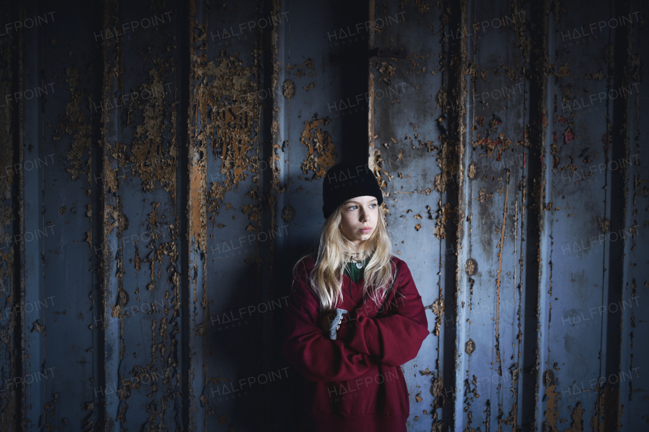 Front view portrait of blond teenager girl standing indoors in abandoned building.