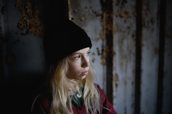 Front view portrait of blond teenager girl standing indoors in abandoned building.